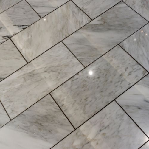White marble tiles with gray veins laid in a diagonal herringbone pattern