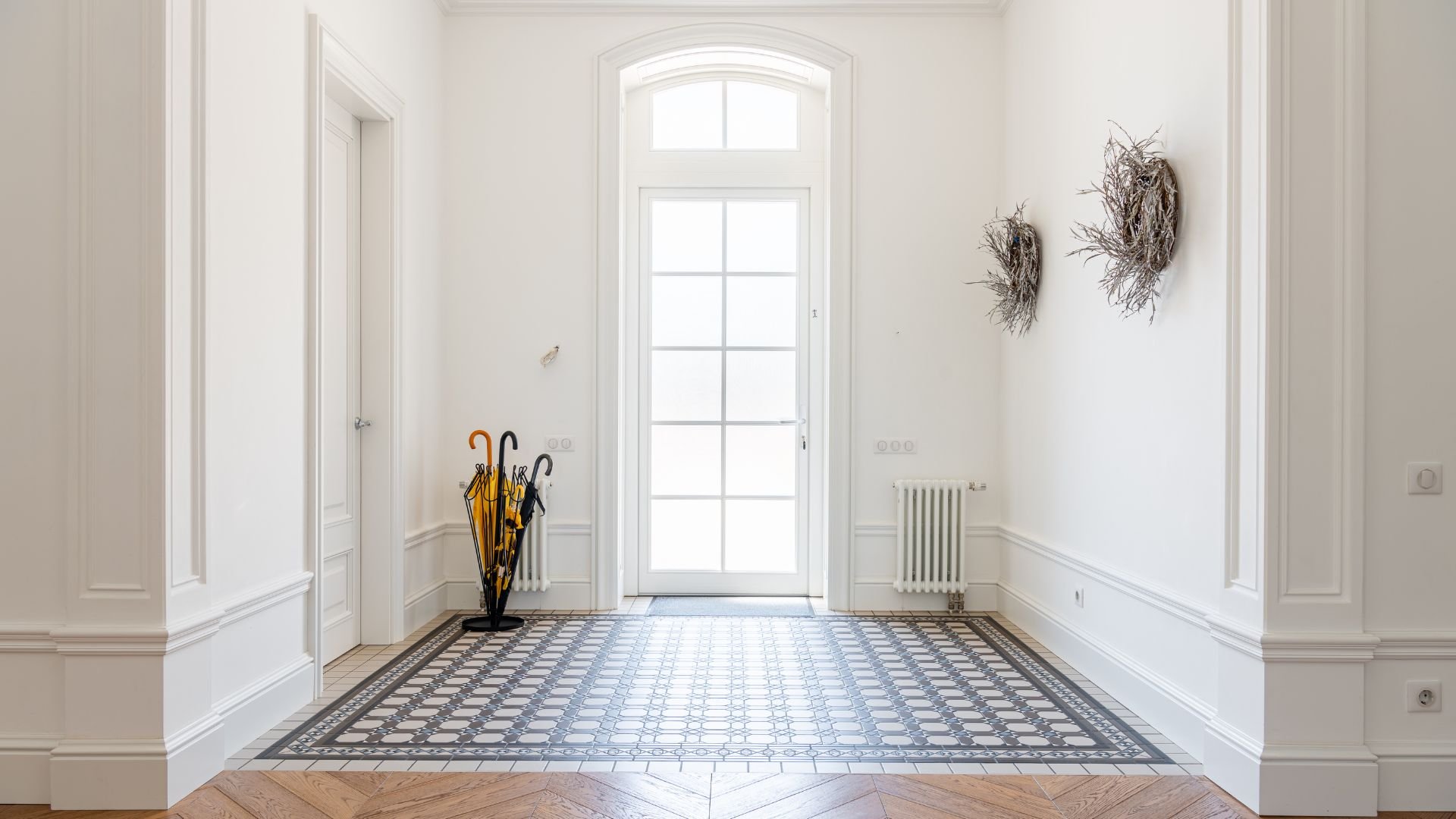 Bright entryway with arched window, umbrella stand, and patterned tile floor