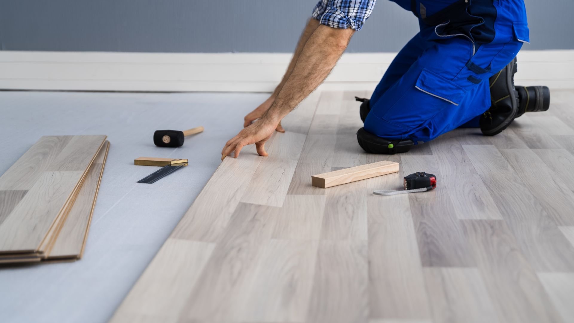 Person installing laminate flooring with tools and wooden planks