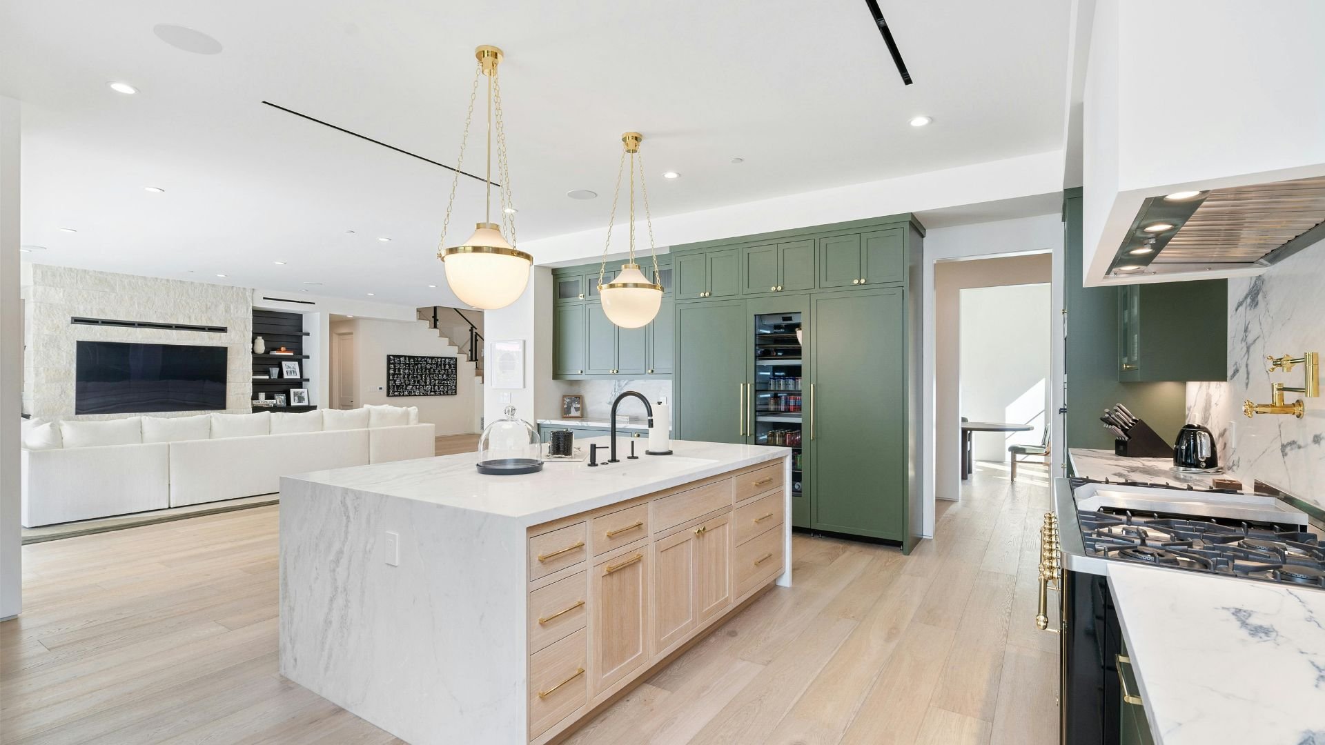 Modern kitchen with green cabinets, marble countertops, and pendant lights